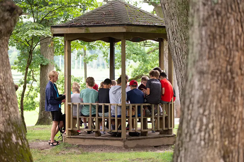 a group of boys and a male counselor do Bible study at a gazebo