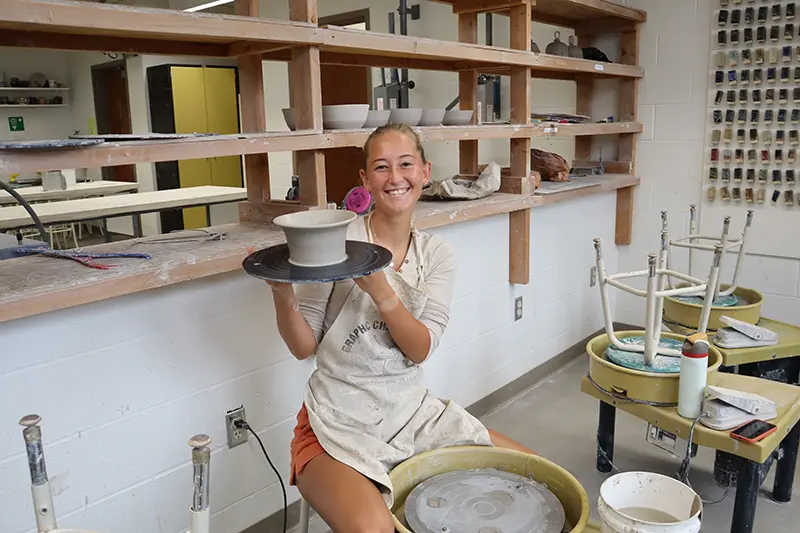 Evie Kerr sits at the wheel and holds her pottery 