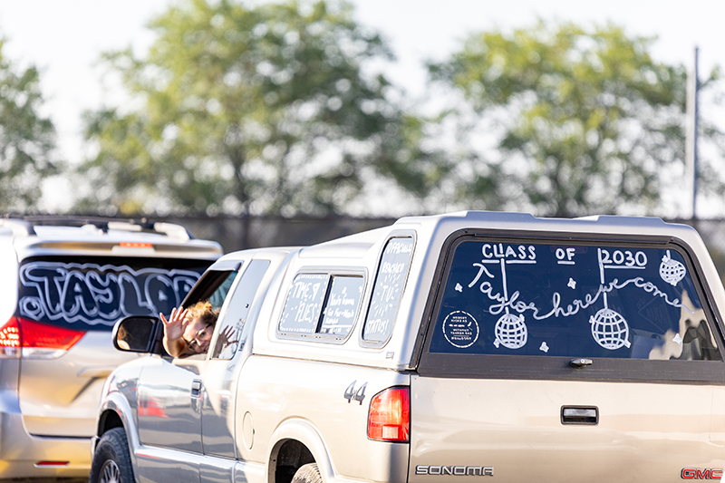 Decorated cars with a car window painted with “Class of 2020” and a person waving from inside.
