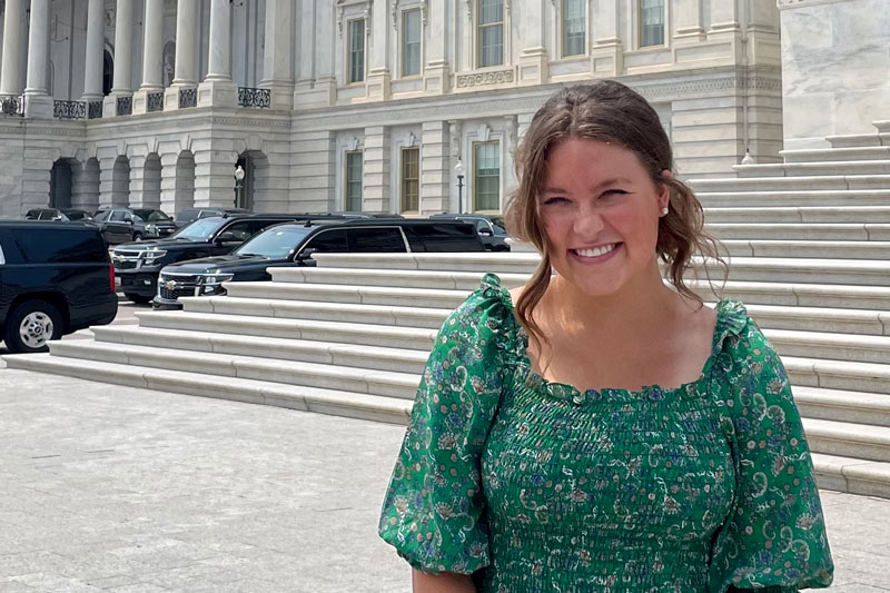 Kyla standing in front of the Capitol with black vehicles next to her